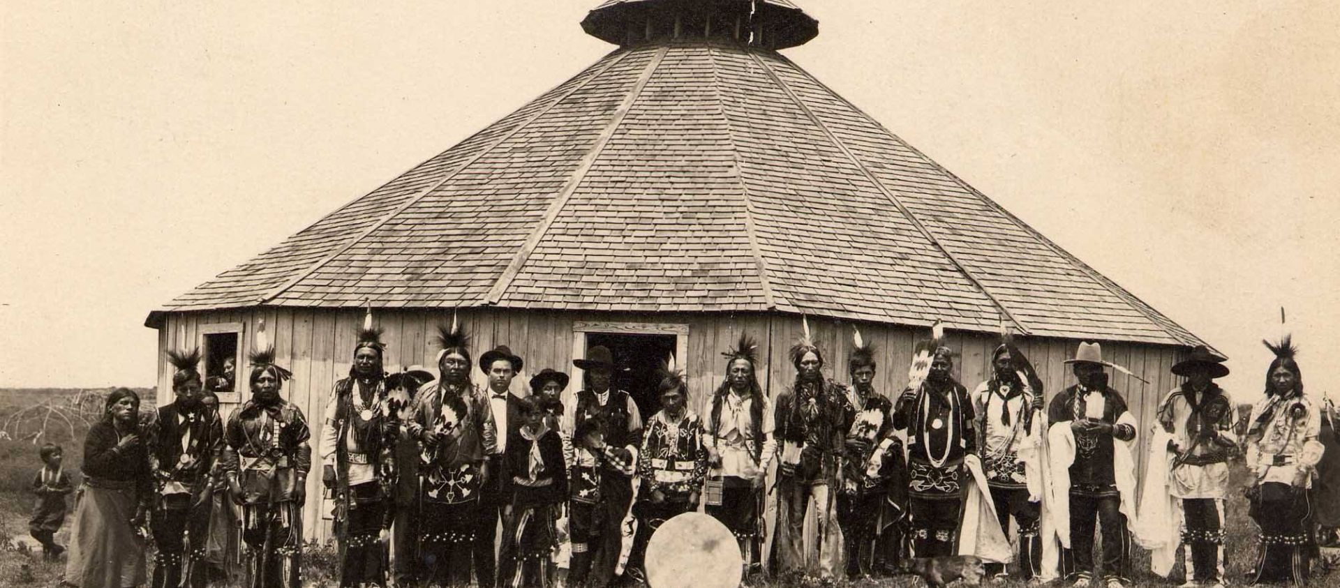 The Inlonshka, has been an important part of Osage life since 1884. The four-day ceremony is celebrated in each Osage district every year in June. This photograph by Vince Dillon shows Osage dancers from the Grayhorse district in 1912 in front of the old roundhouse.